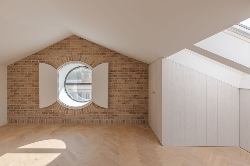 Exposed brick gable wall with circular window flanked by white shutters under the eaves