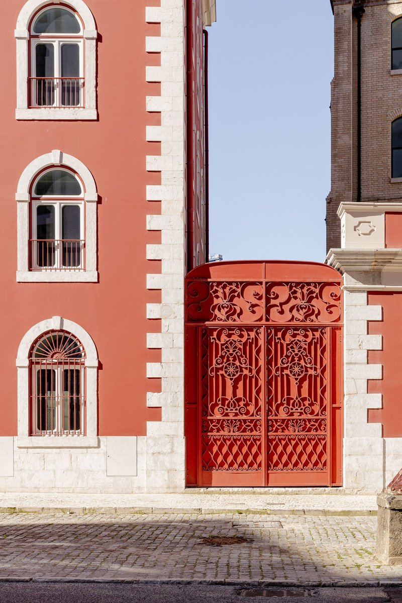 Ornamental red metal elevator enclosure adjacent to a red brick wall with white-trimmed arched windows