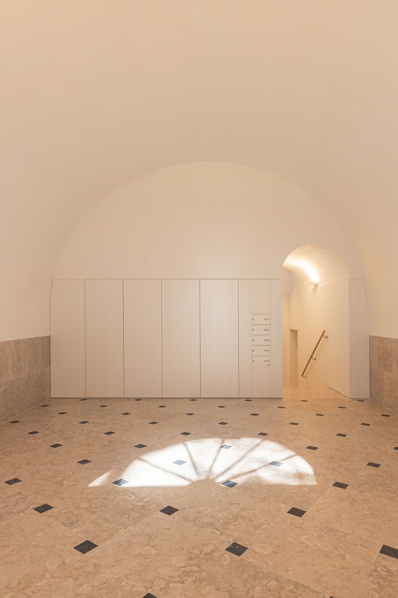 Vaulted entry space with white paneled wall and patterned terrazzo floor casting arched window shadows