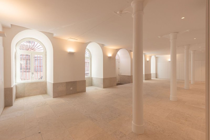 Open floor with white columns and arched windows lined with stone wainscoting in soft light