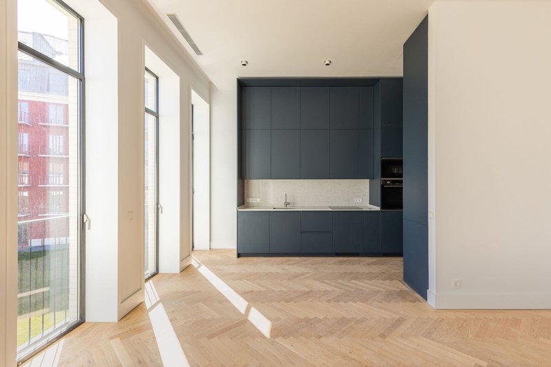Kitchen with dark blue cabinetry and limestone countertop adjoining oak herringbone floor in daylight