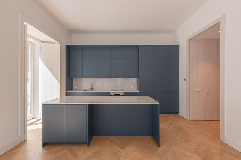 Kitchen island with dark blue panels and stone top beneath vaulted ceiling with timber door