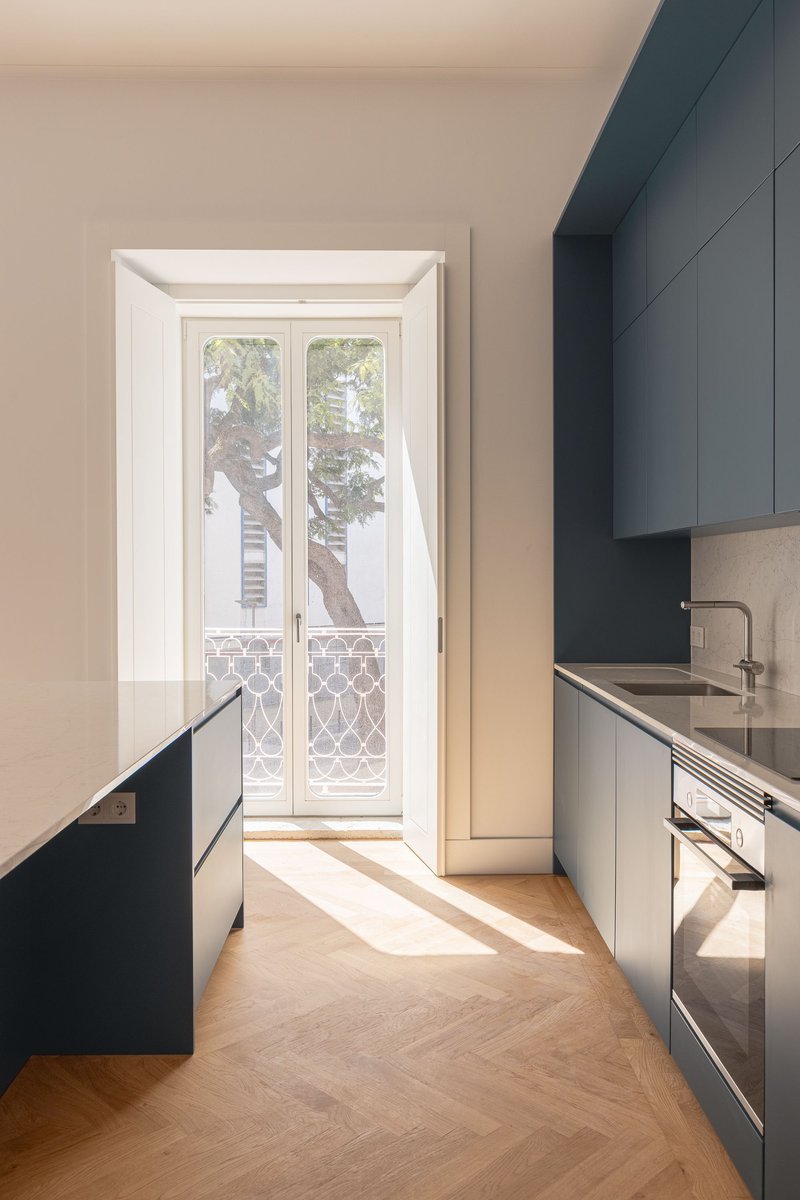 Kitchen with blue-grey cabinetry and French doors framing a tree-lined balcony in afternoon light
