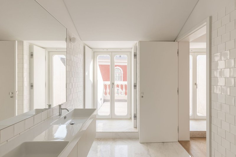 White-tiled bathroom with twin sinks and glazed doors opening to a room with a red facade beyond