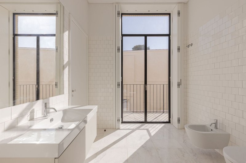Bathroom with white subway tiles and glass door opening onto a narrow terrace with metal railing