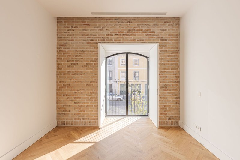 Arched window set in exposed brick wall with herringbone oak flooring and sunlight streaming across the room
