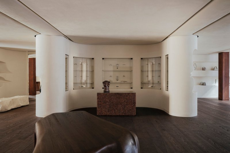 Curved wall with recessed glass vitrines flanking a central red granite counter beneath indirect cove lighting
