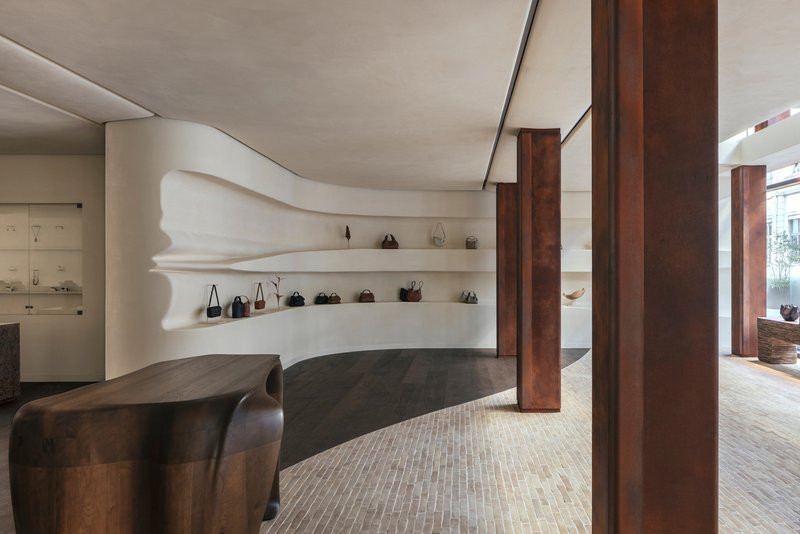 Sculpted white plaster shelving with undulating edges displaying handbags between dark timber columns