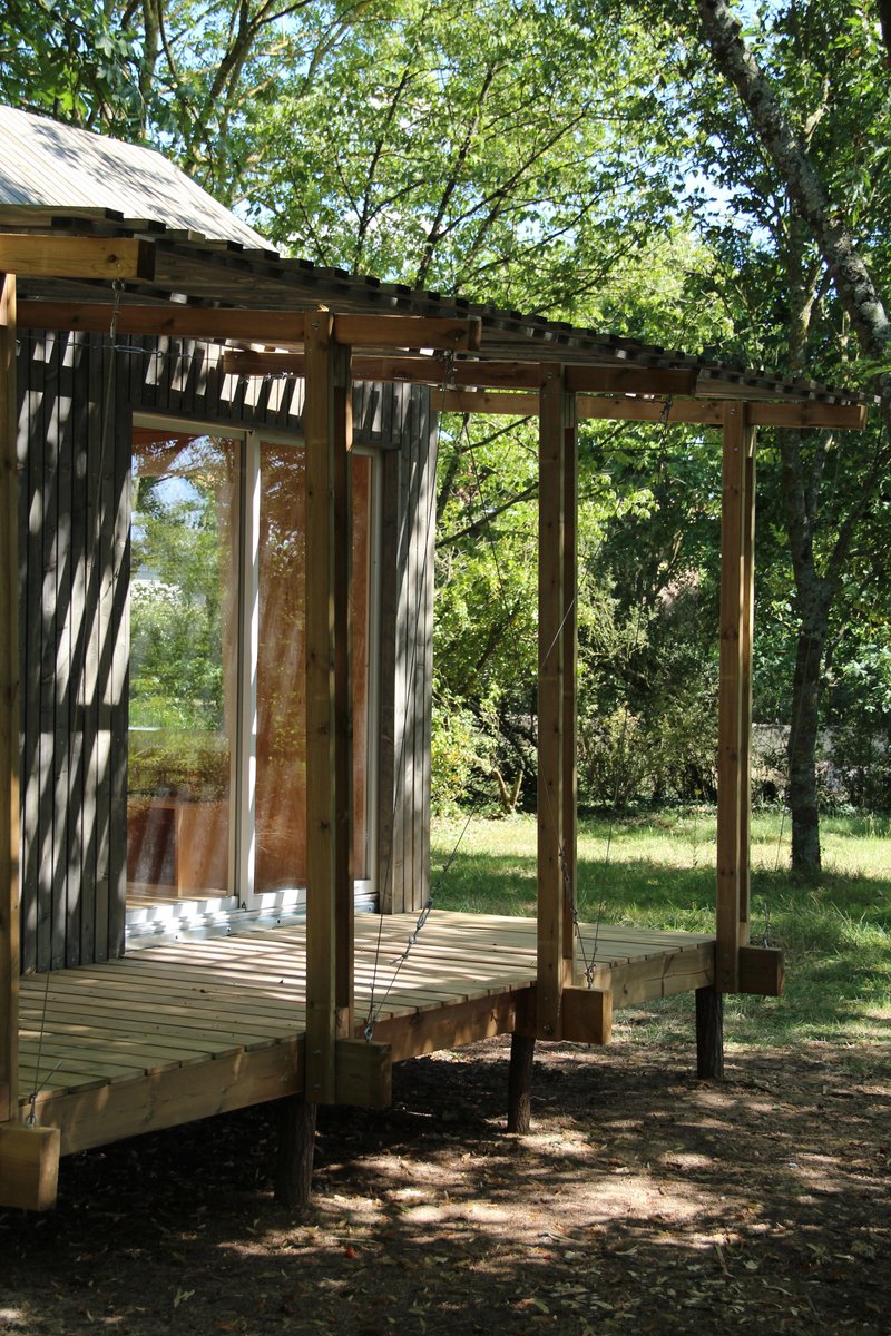 Timber-framed pavilion with exposed rafters and decking beneath dappled tree canopy