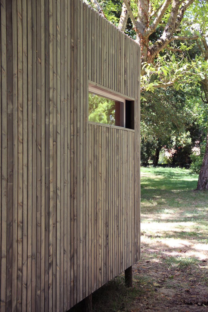 Vertical timber slat facade with single punched window opening among sunlit trees