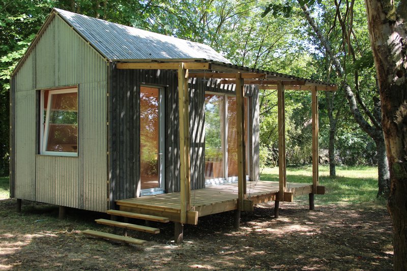 Timber-framed deck extension with open pergola structure attached to the metal-clad cabin under tree canopy