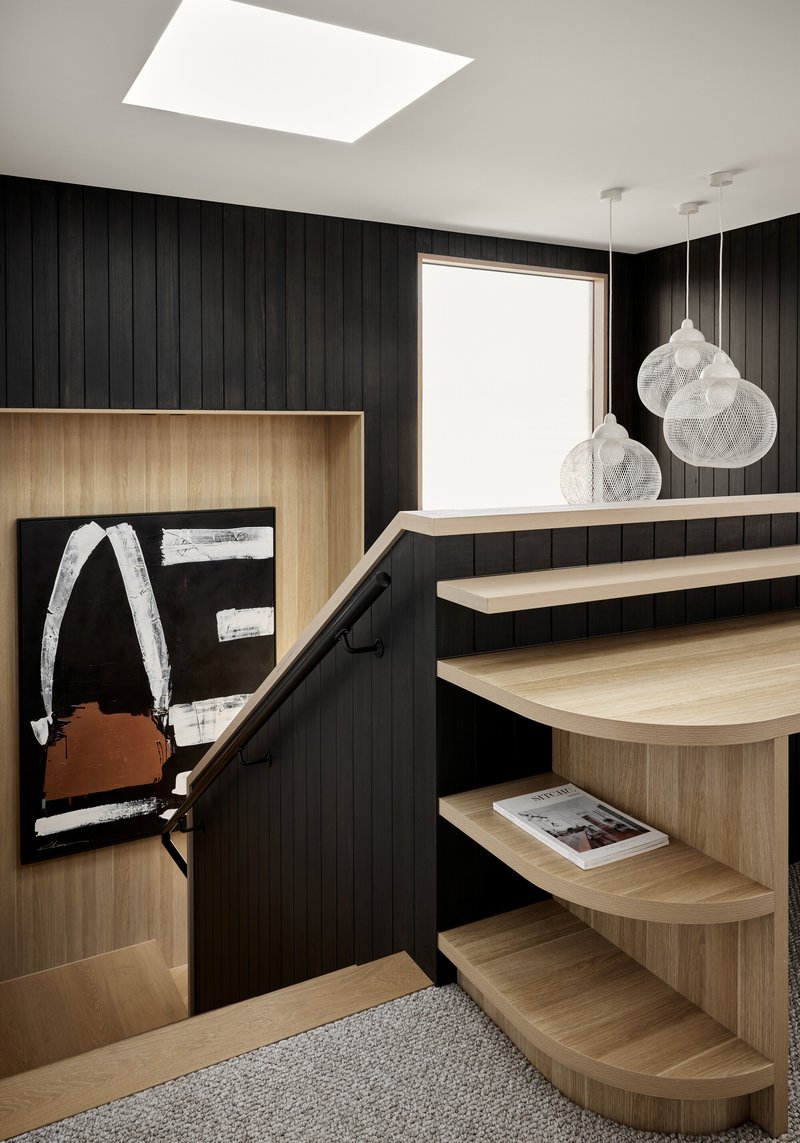 Curved timber stair treads against a black vertical panel wall with mesh pendant lights overhead