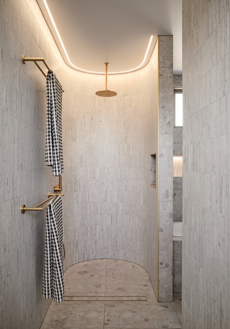 Curved shower niche with integrated ceiling lighting and brass rainfall head above patterned floor tile