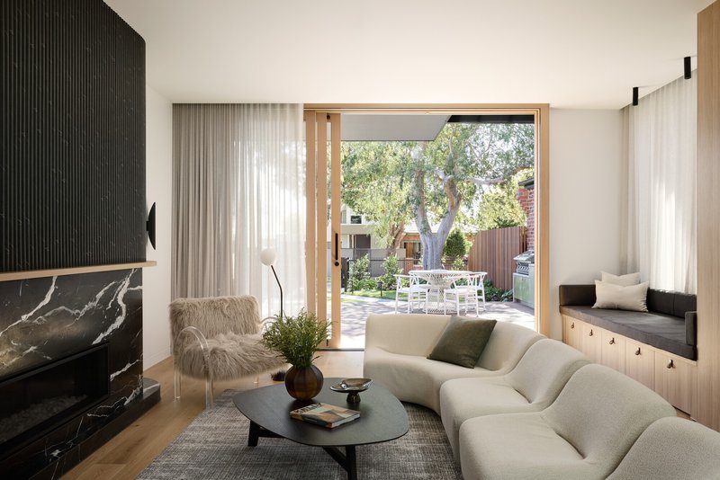 Living room with sheer curtains framing a timber-lined door opening to the garden and outdoor terrace beyond