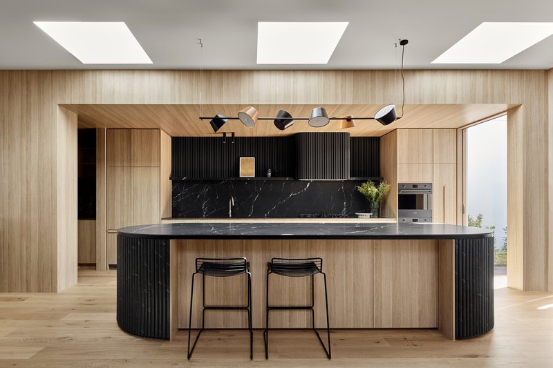 Kitchen island with black marble countertop under three rectangular skylights and timber-clad walls and ceiling