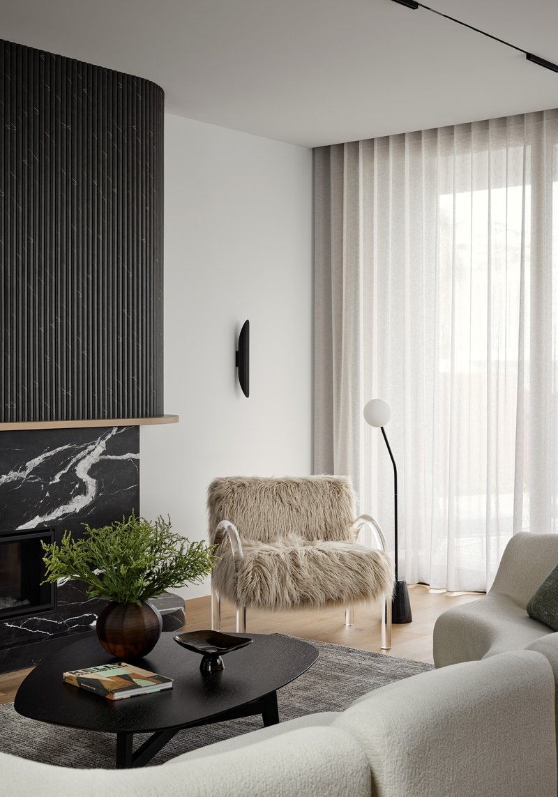 Living room fireplace surround in black marble with vertical batten hood and sheer curtains filtering daylight