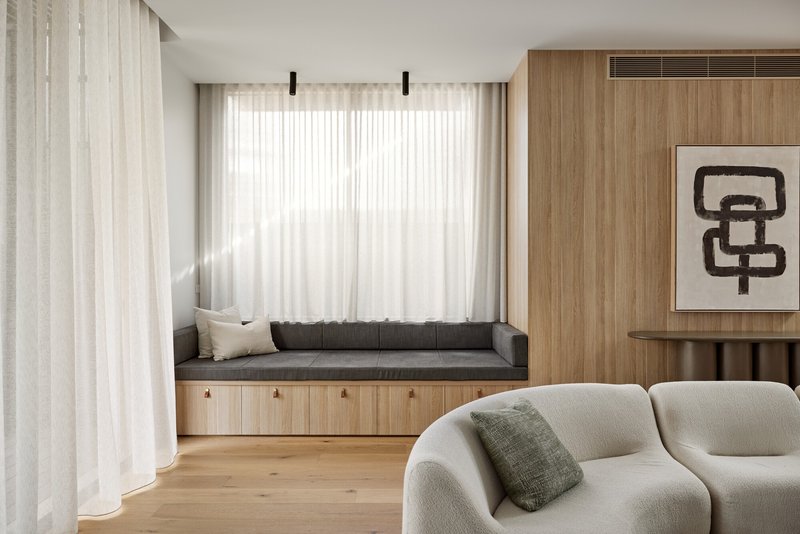 Built-in window seat with timber storage below and sheer curtains filtering soft natural light