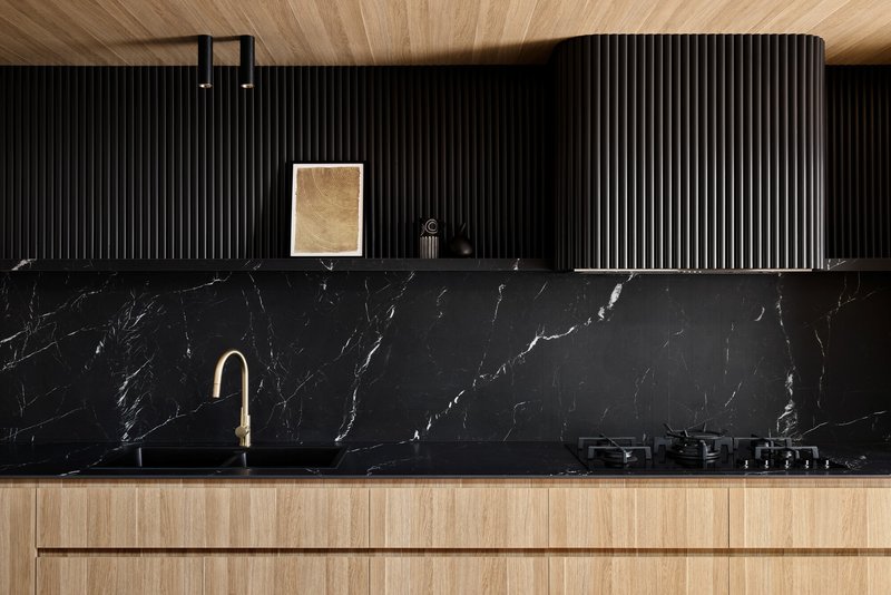 Black marble backsplash with vertical fluted cabinetry above timber base units