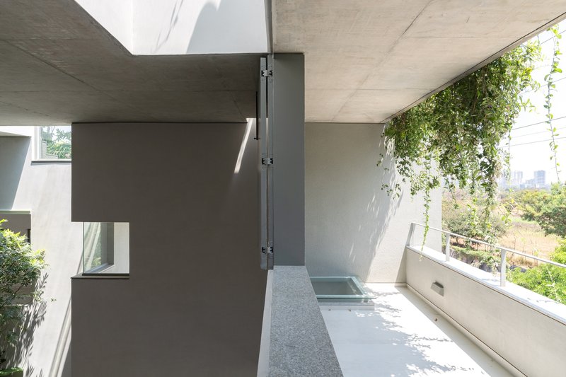Covered terrace with exposed concrete ceiling, terrazzo flooring, and hanging vines filtering daylight