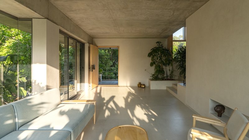Living room with concrete ceiling, polished concrete floor, timber furniture, and dappled sunlight from garden
