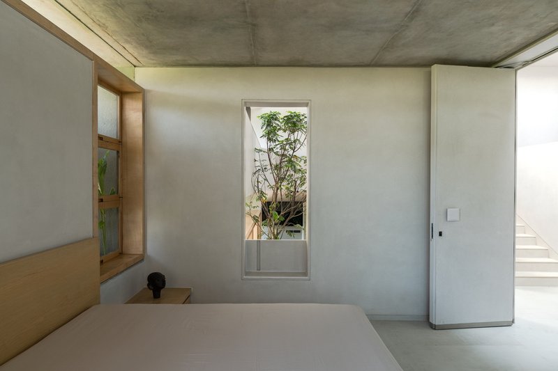 Bedroom corner with pivoting window opening to a planted courtyard and timber shelving detail