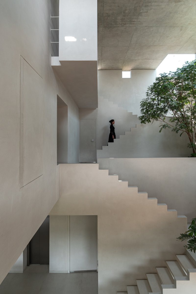Interlocking white stairs around a planted courtyard with a figure ascending the upper flight