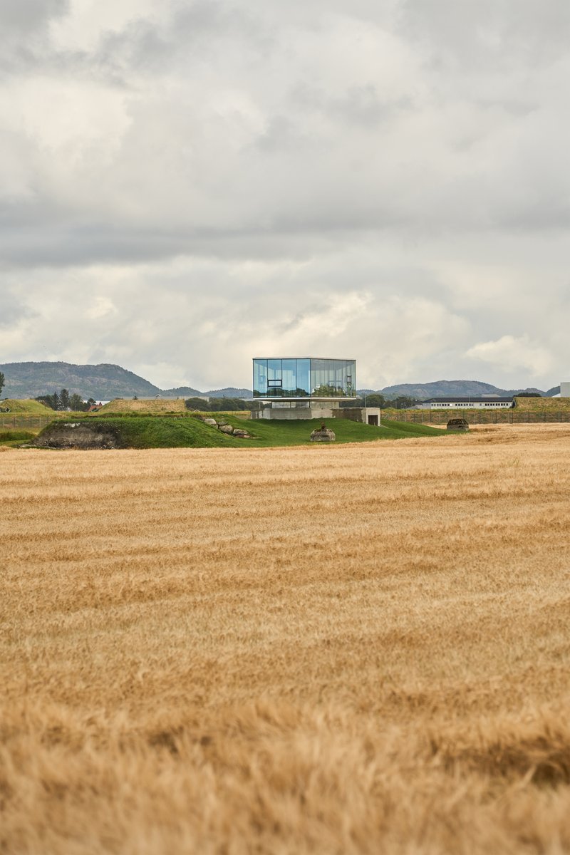 Distant view of the cantilevered structure in harvested fields beneath a heavy cloud cover and hills