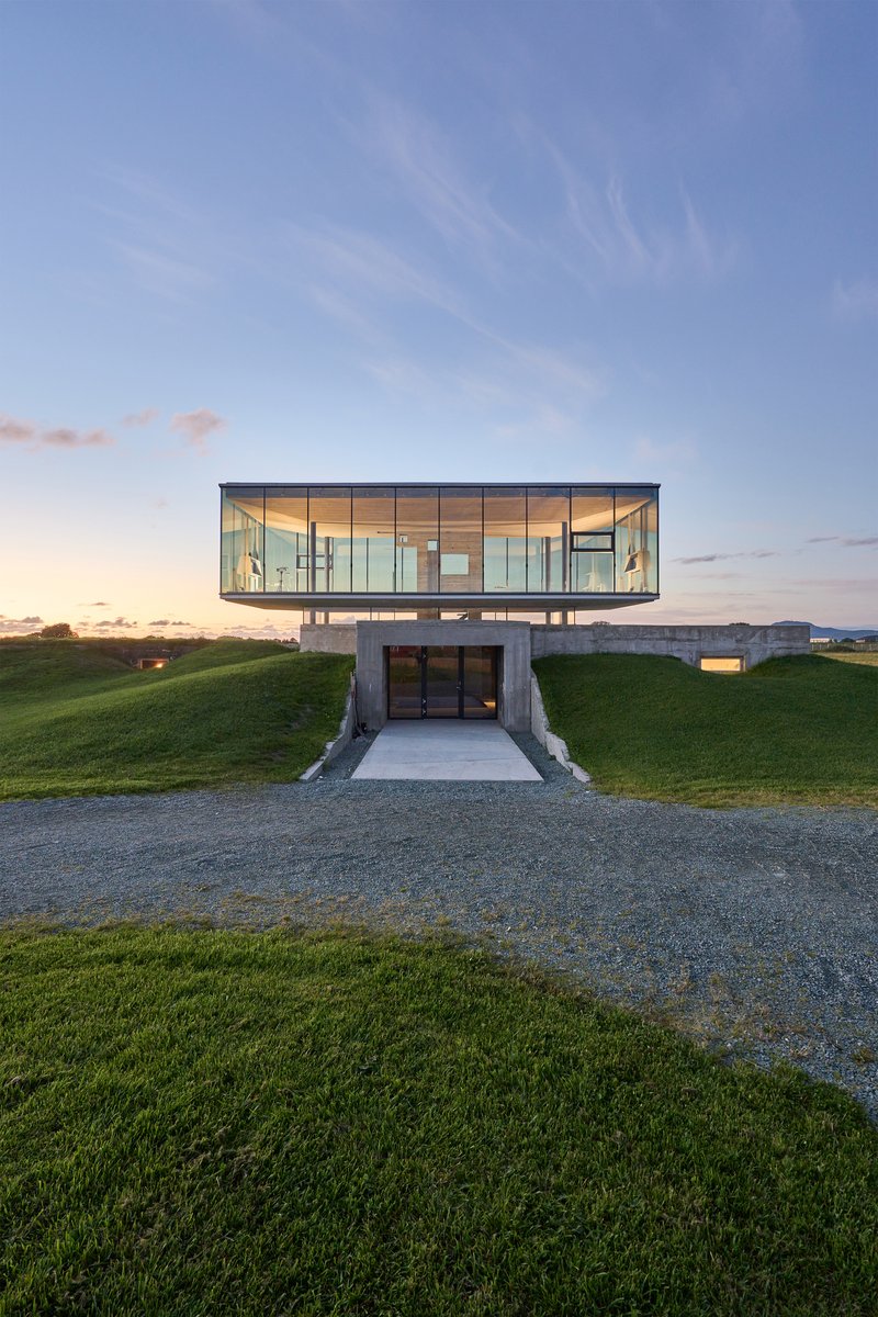 Frontal view of the glass volume cantilevered above a recessed concrete entrance at dusk