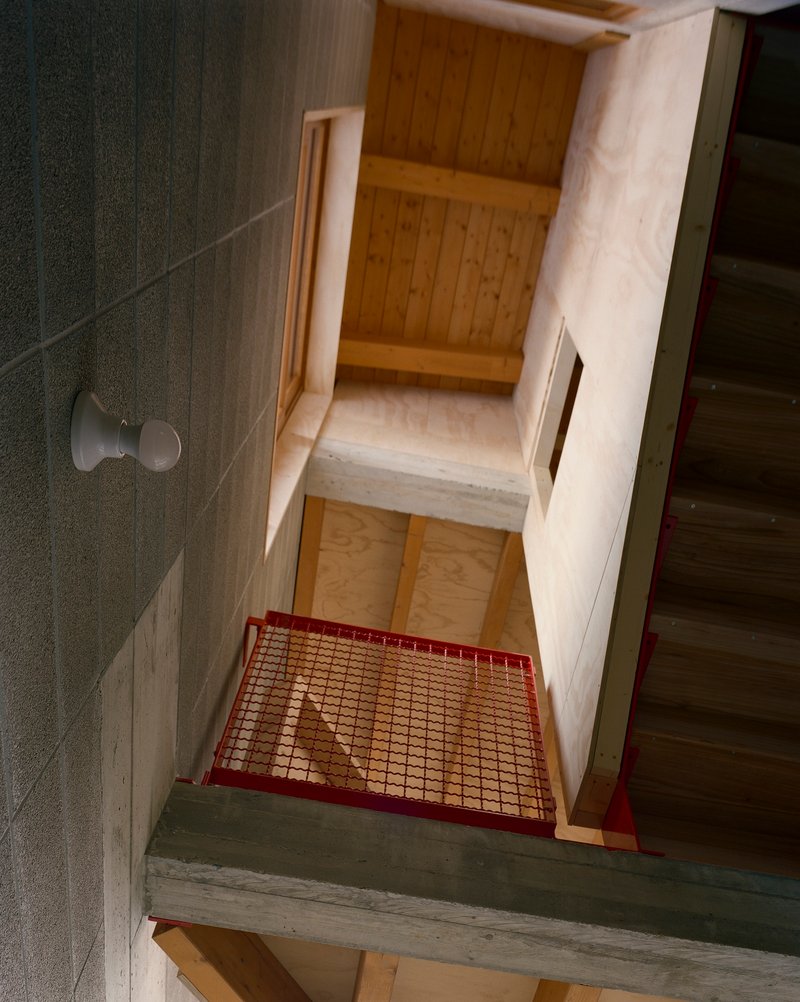 Top-down view of a timber staircase with red mesh safety railing between concrete and plywood walls