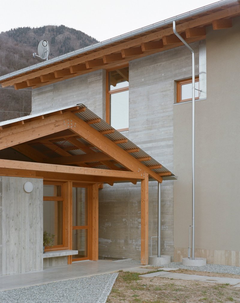 Entrance porch with exposed timber beams and concrete wall beside a wooded slope