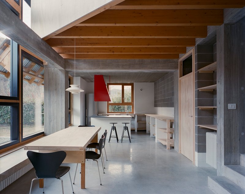 Open-plan kitchen and dining area with exposed timber joists and concrete beams under daylight
