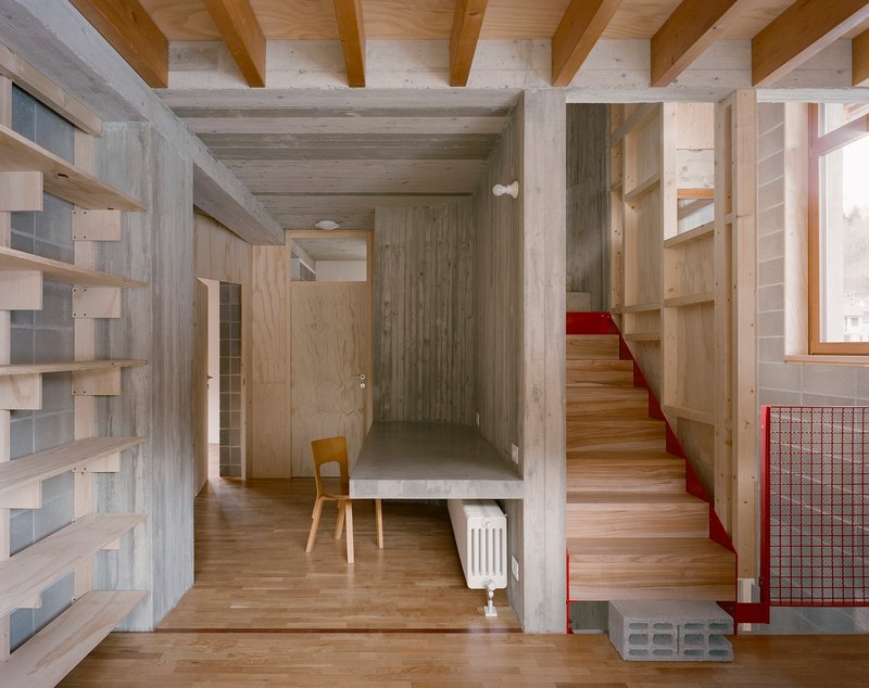 Entry hall with timber stair featuring red metal handrail and concrete structural frame