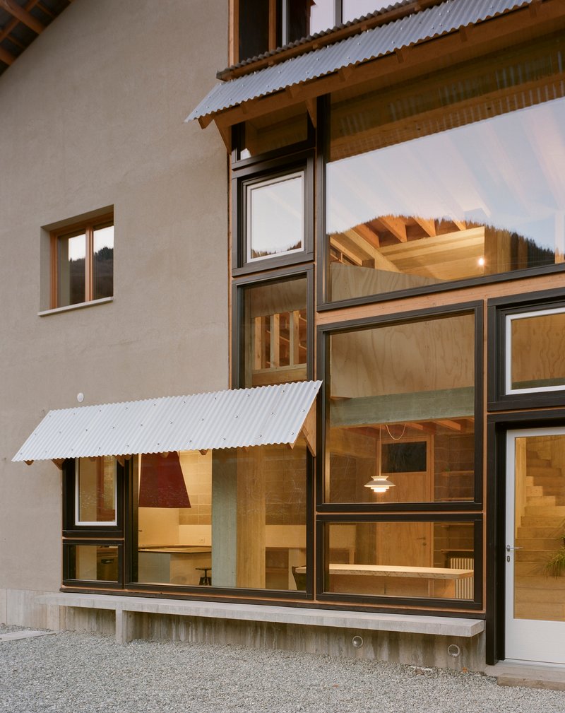 Exterior facade with timber-framed windows and corrugated metal awnings illuminated at dusk