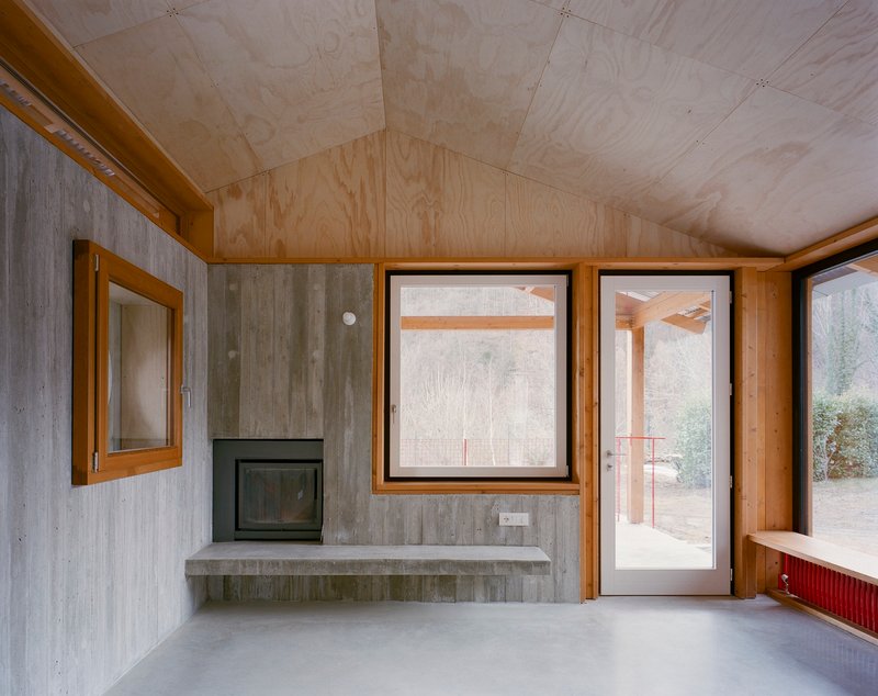 Interior room with plywood ceiling, board-formed concrete walls, and a corner fireplace