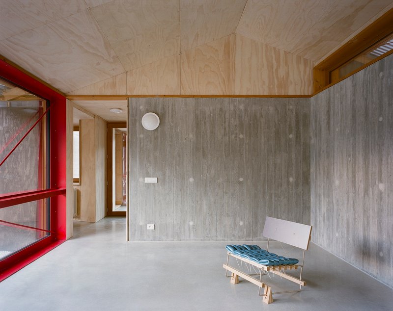 Living space with plywood ceiling and board-formed concrete walls featuring a lounge chair