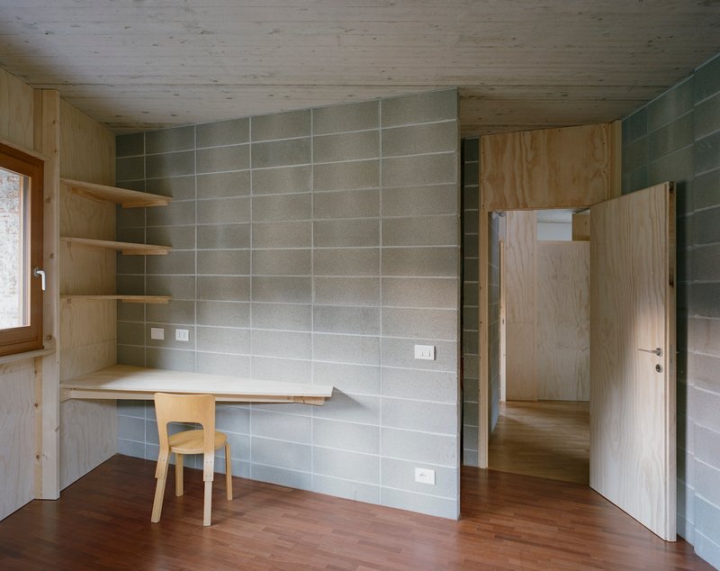 Workspace with built-in plywood desk and corner shelving against concrete block walls