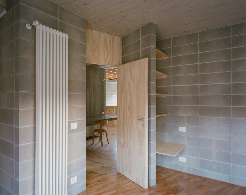 Interior room with concrete block walls, light plywood built-in shelving, and a white vertical radiator