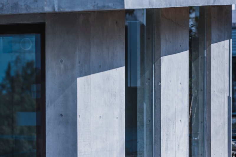 Close-up of concrete walls intersecting with steel-framed glass panels reflecting afternoon light