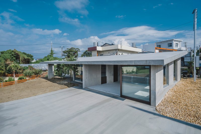 Single-story concrete pavilion with flat roof and glass walls overlooking a gravel courtyard