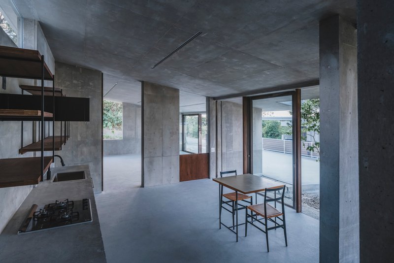Open plan interior with concrete columns and ceiling, dining table near glazed doors opening to courtyard