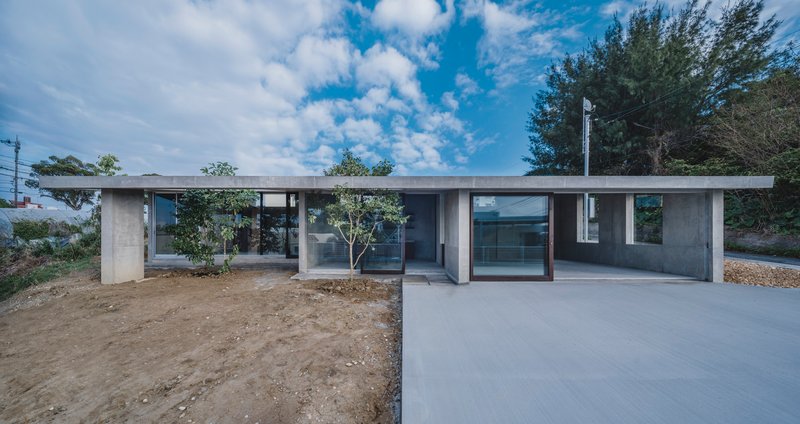 Front facade with concrete columns framing glazed openings and young planted trees under blue sky