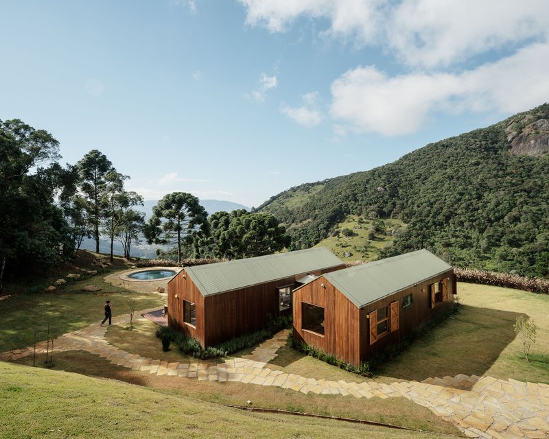 Aerial view of two timber-clad gabled volumes with metal roofs set on a hillside lawn with pool