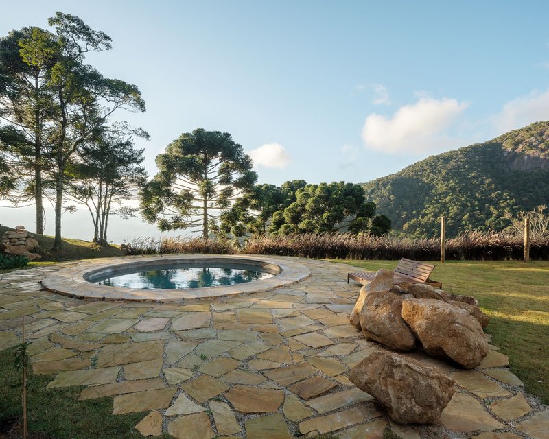 Circular pool surrounded by flagstone paving with boulders and grasses facing forested hills