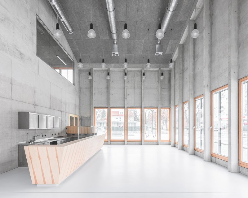 Interior lobby with faceted timber reception desk, exposed concrete walls, ceiling ducts and pendant lights
