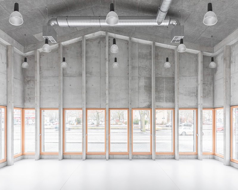 Curved interior corner with rhythmic concrete fins between timber-framed windows under exposed ductwork and pendant lights