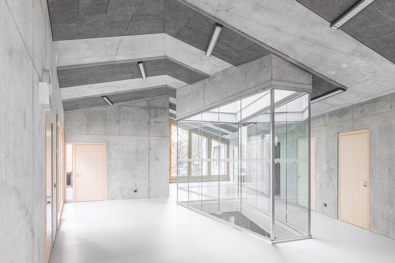 Interior hall with glass-walled enclosure beside concrete walls and stepped ceiling beams overhead