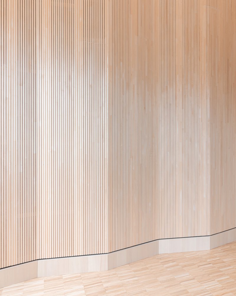 Detail of vertical timber slat wall with curved corner meeting pale wood flooring