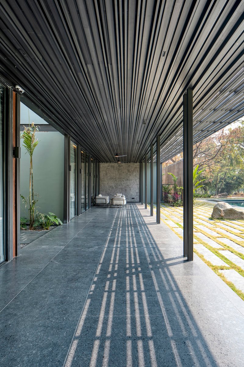 Covered porch with slatted metal ceiling casting shadows across the stone floor at midday