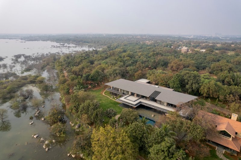Aerial view of the grey-roofed residence nestled among dense forest and adjacent wetlands under hazy skies