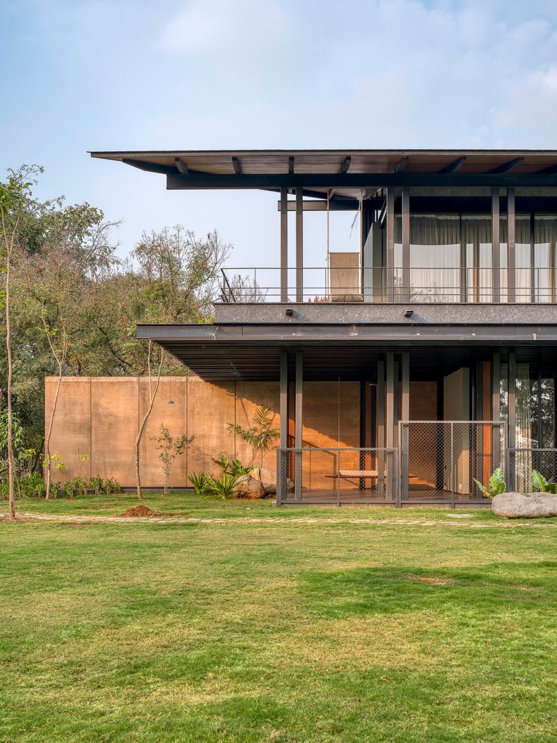 Two-story steel-framed facade with deep overhangs and rammed earth wall beside a manicured lawn